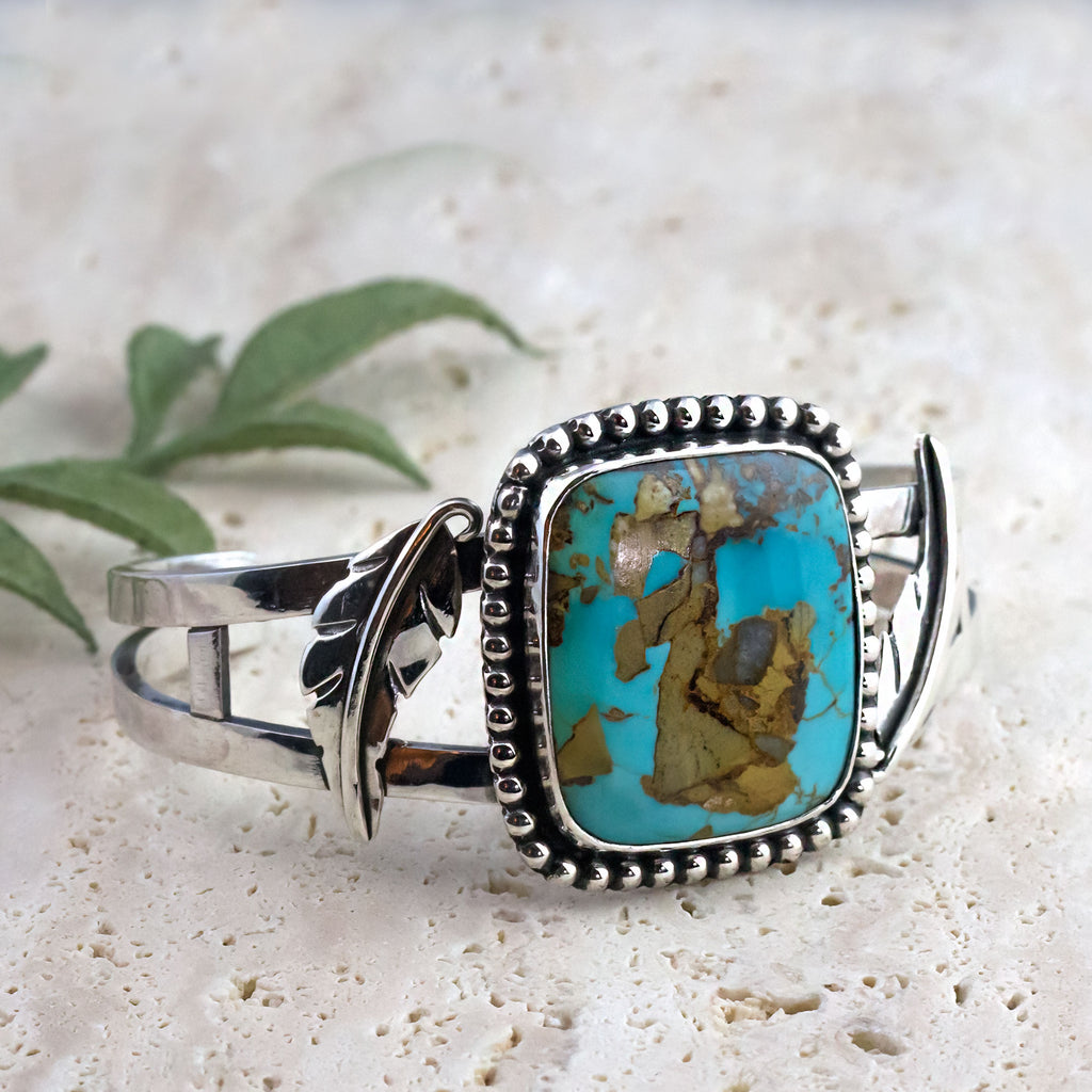 Silver-tone cuff bracelet featuring turquoise and brown oval stone with beaded frame