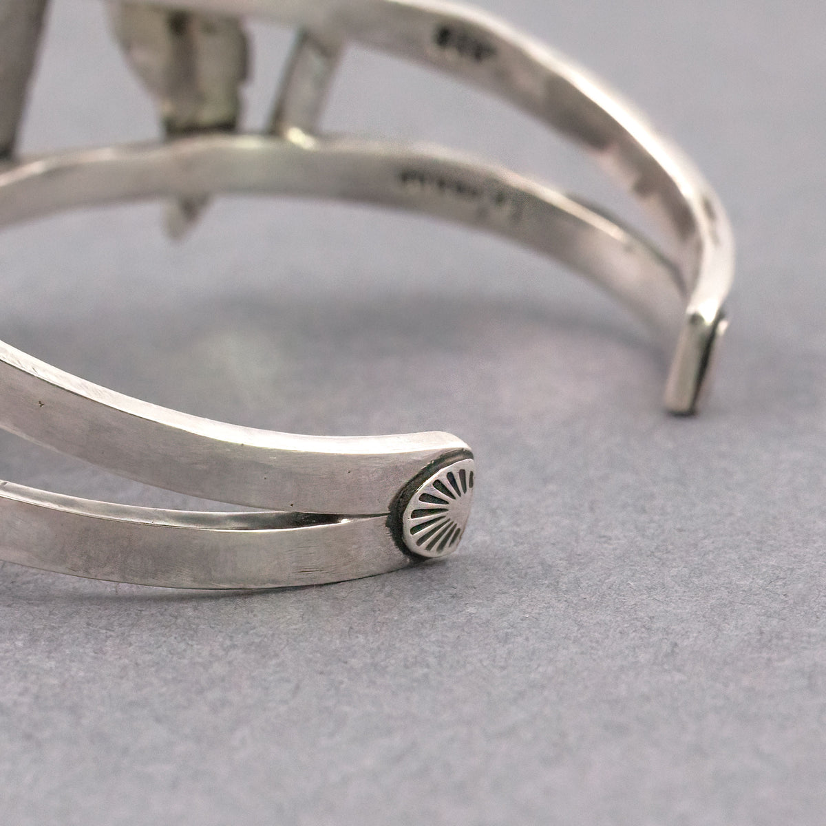 Close-up of silver-tone cuff bracelet end with small sunburst detail